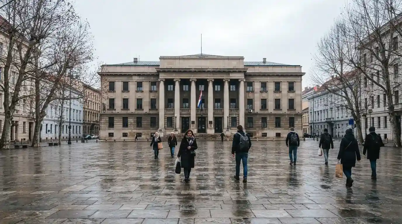 Trg ispred državne zgrade s hrvatskom zastavom, ljudi prolaze u zimskim kaputima, hladno jutarnje svjetlo.